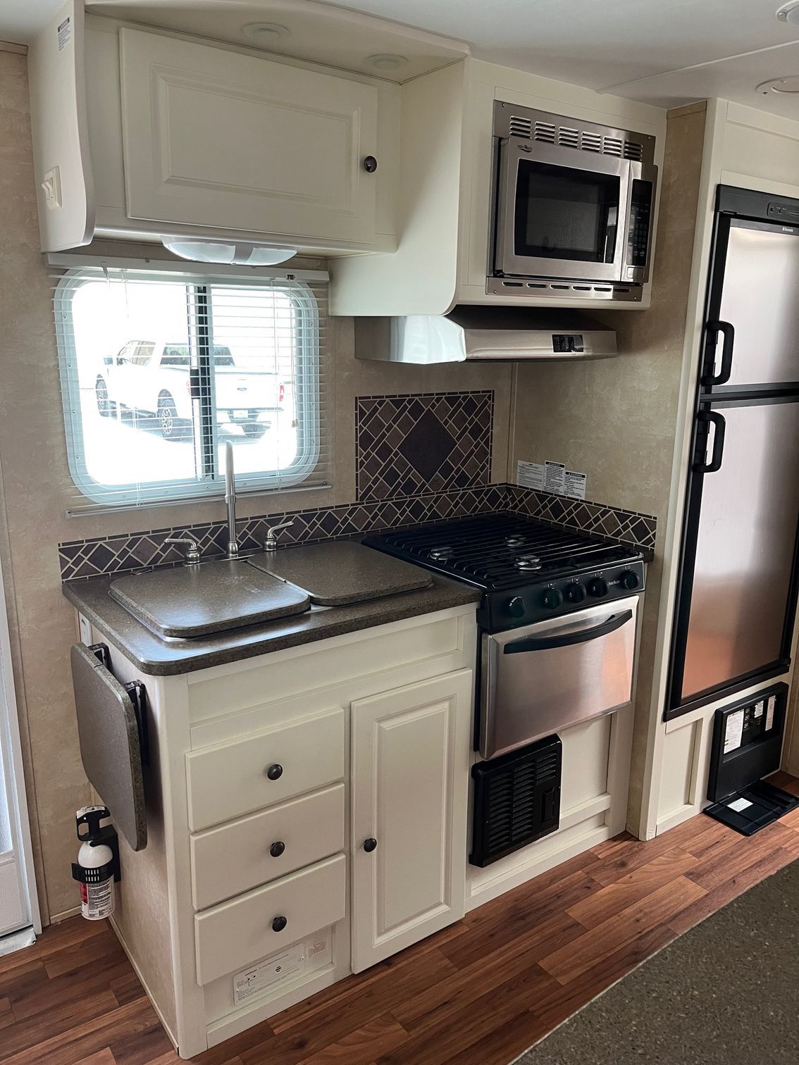 Compact RV kitchen with white cabinets, stainless sink, stove, microwave, and wood flooring