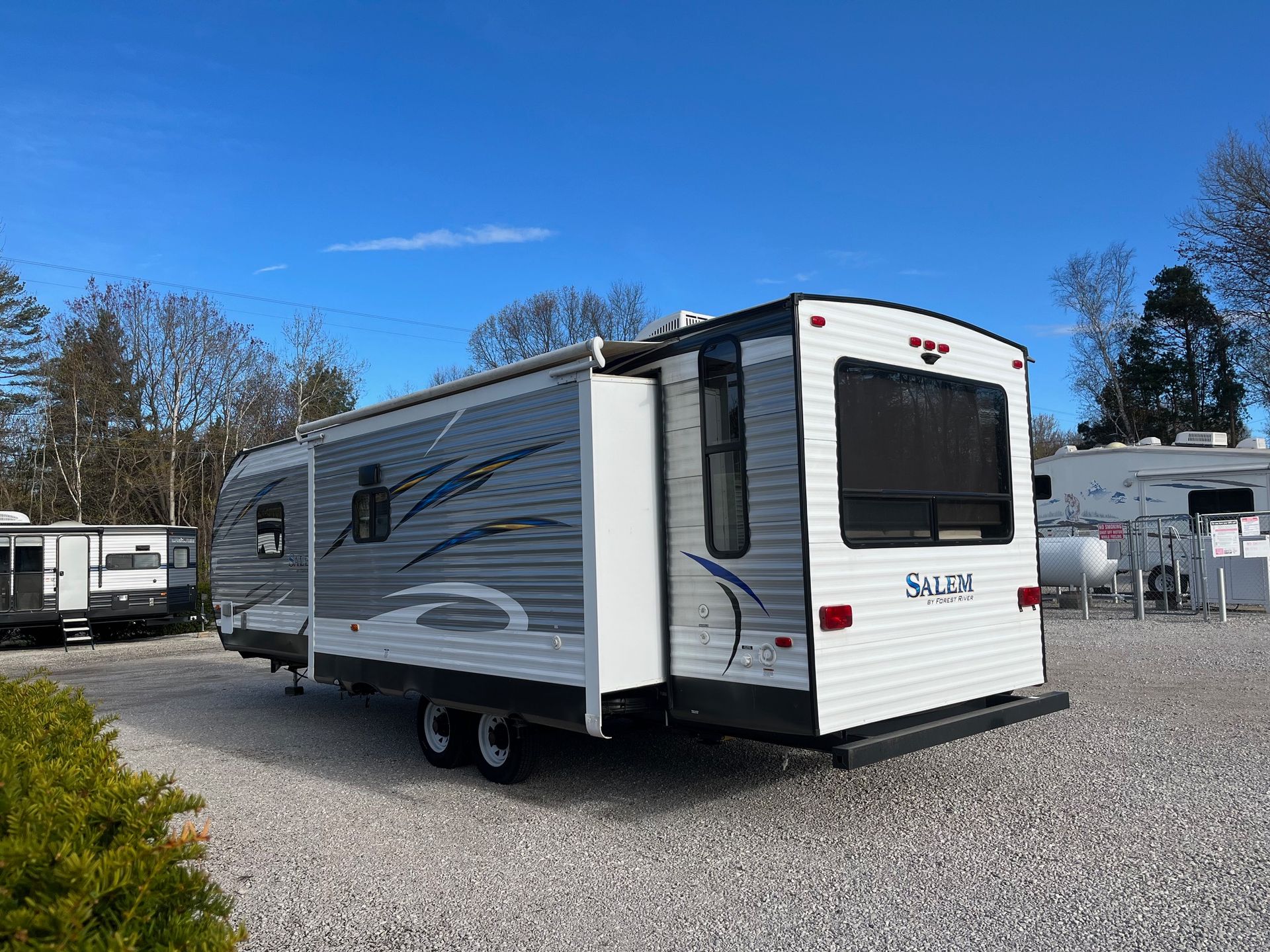 White and gray travel trailer parked on gravel under a blue sky