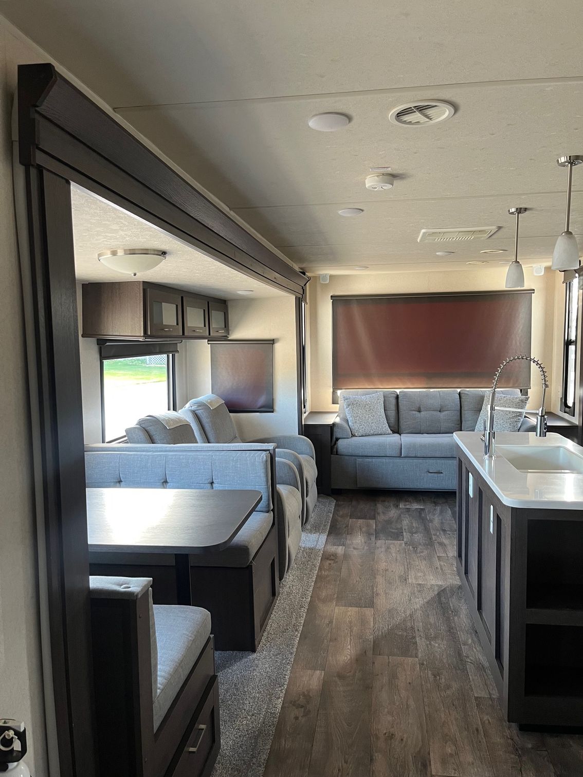 Compact RV interior with gray sofas, kitchen counters, wood flooring, and overhead cabinets