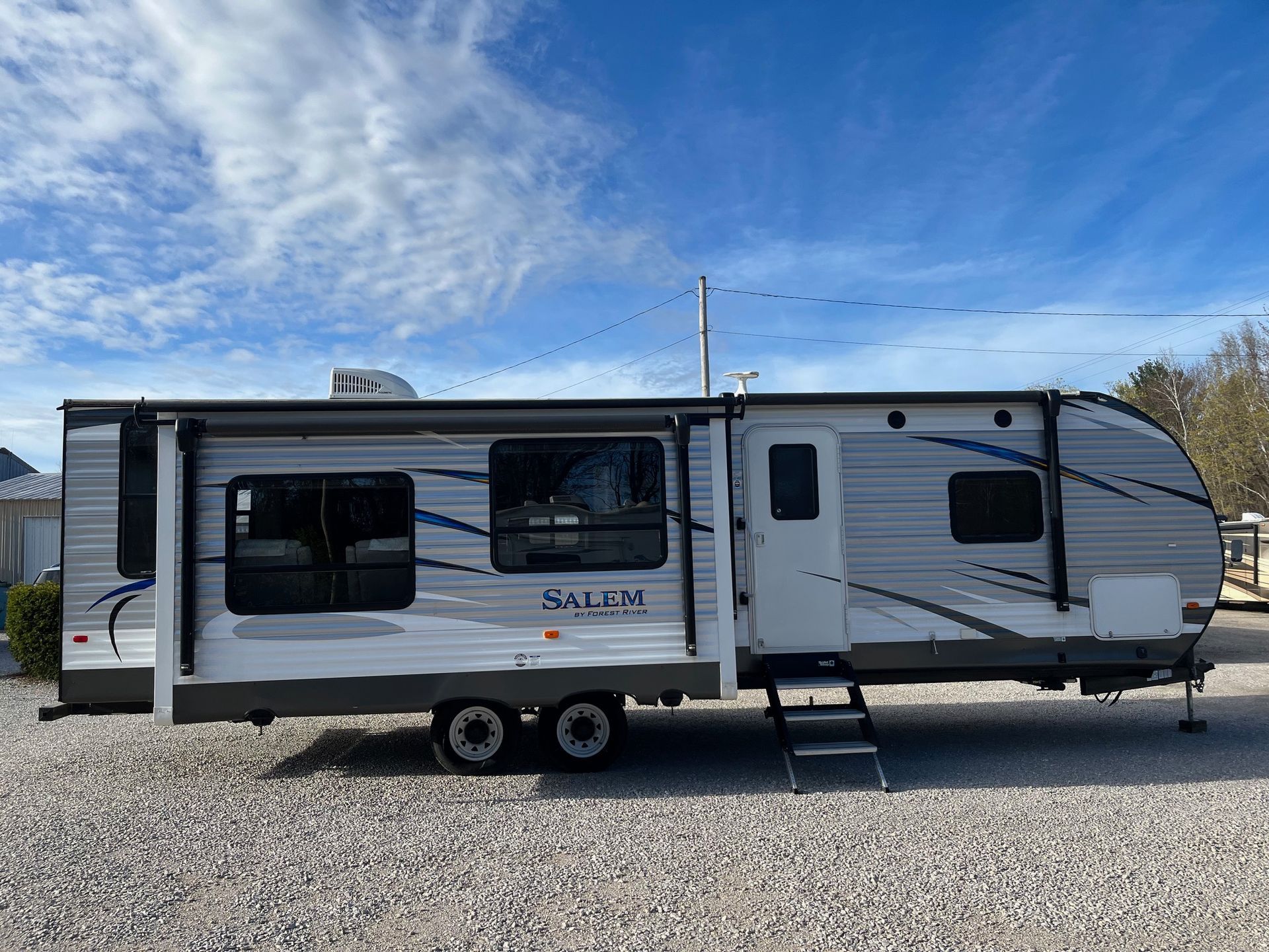 White travel trailer with slide-outs parked on gravel under a blue sky.