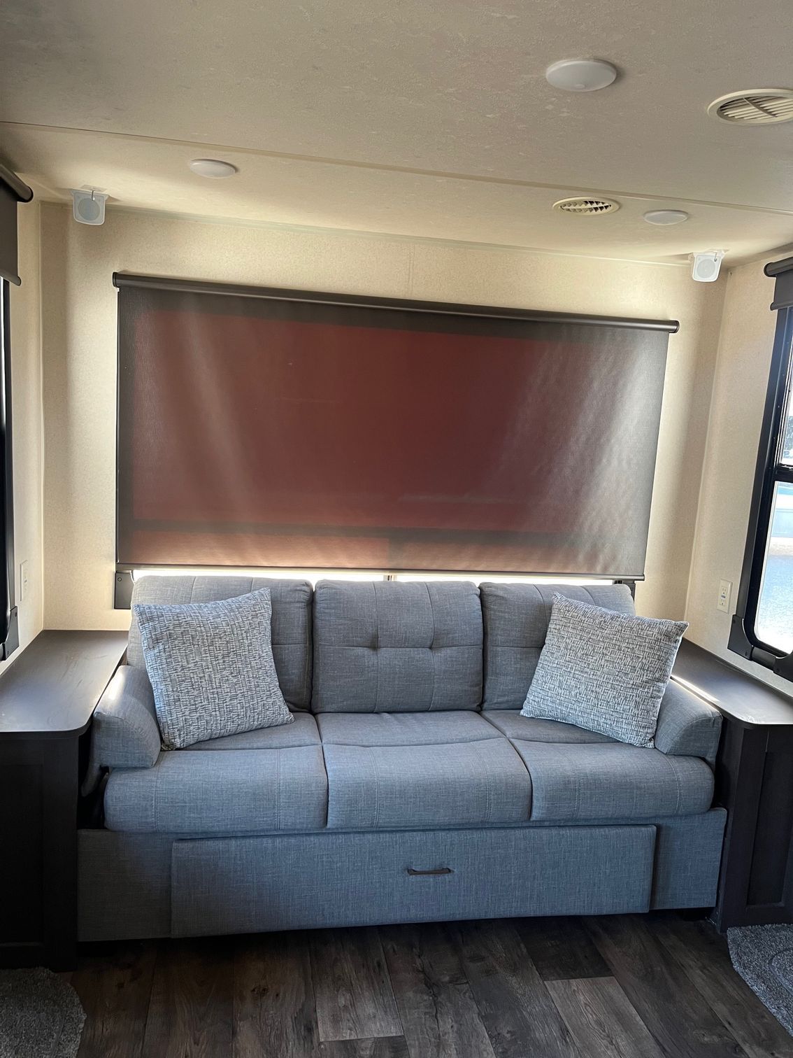 Gray sofa with patterned pillows beneath a closed window blind in a small RV or camper seating area
