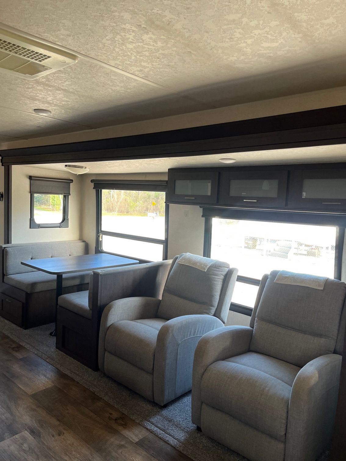 RV living area with two gray recliners, a bench seat, and side windows