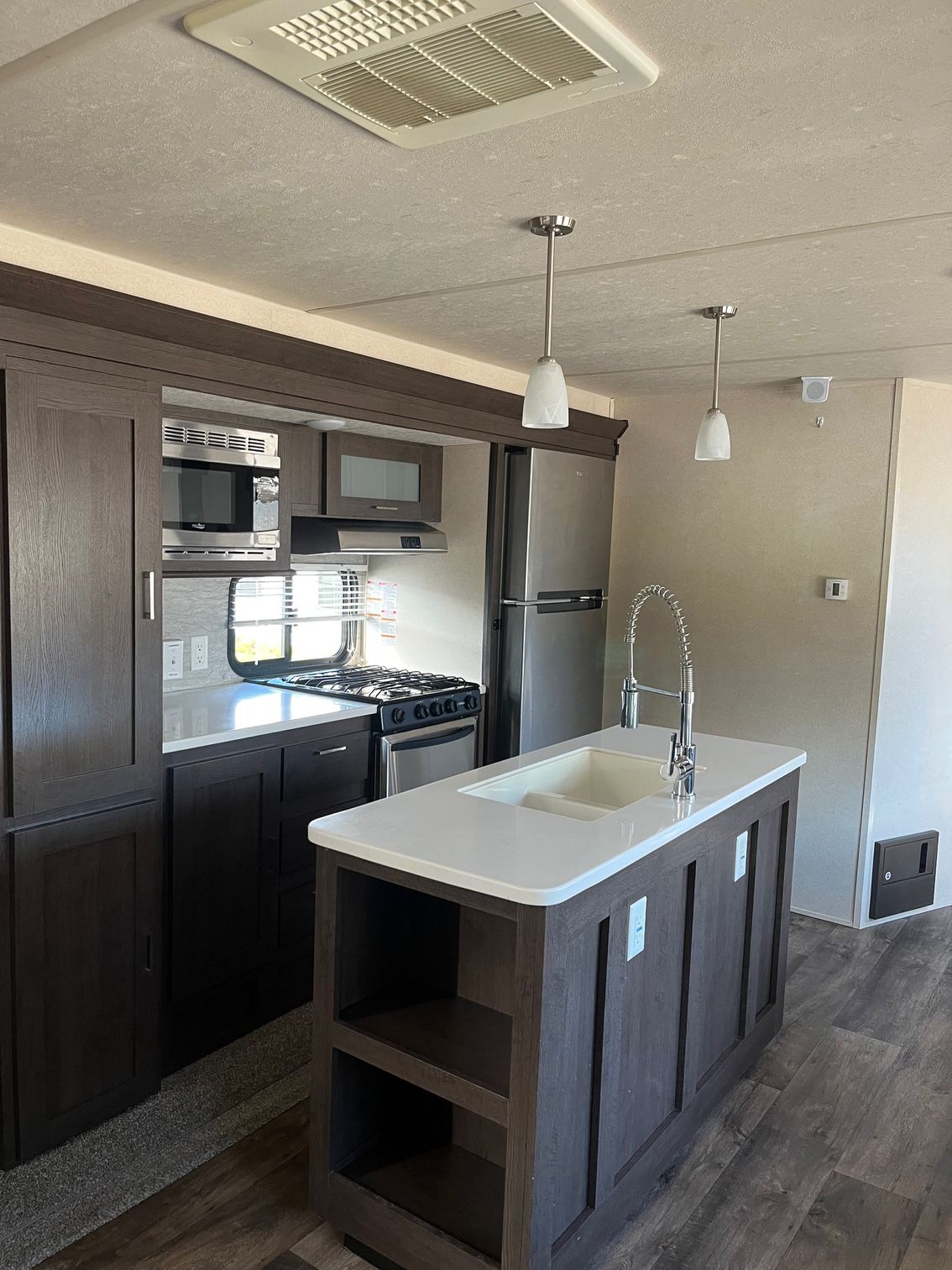 Modern kitchen with dark cabinets, stainless appliances, and a central island with a white sink.