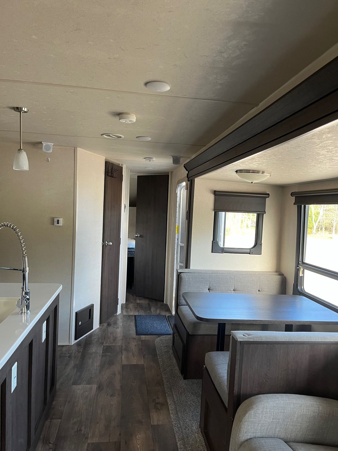 RV interior with booth dining area, sofa, and compact kitchen along wood-floored aisle