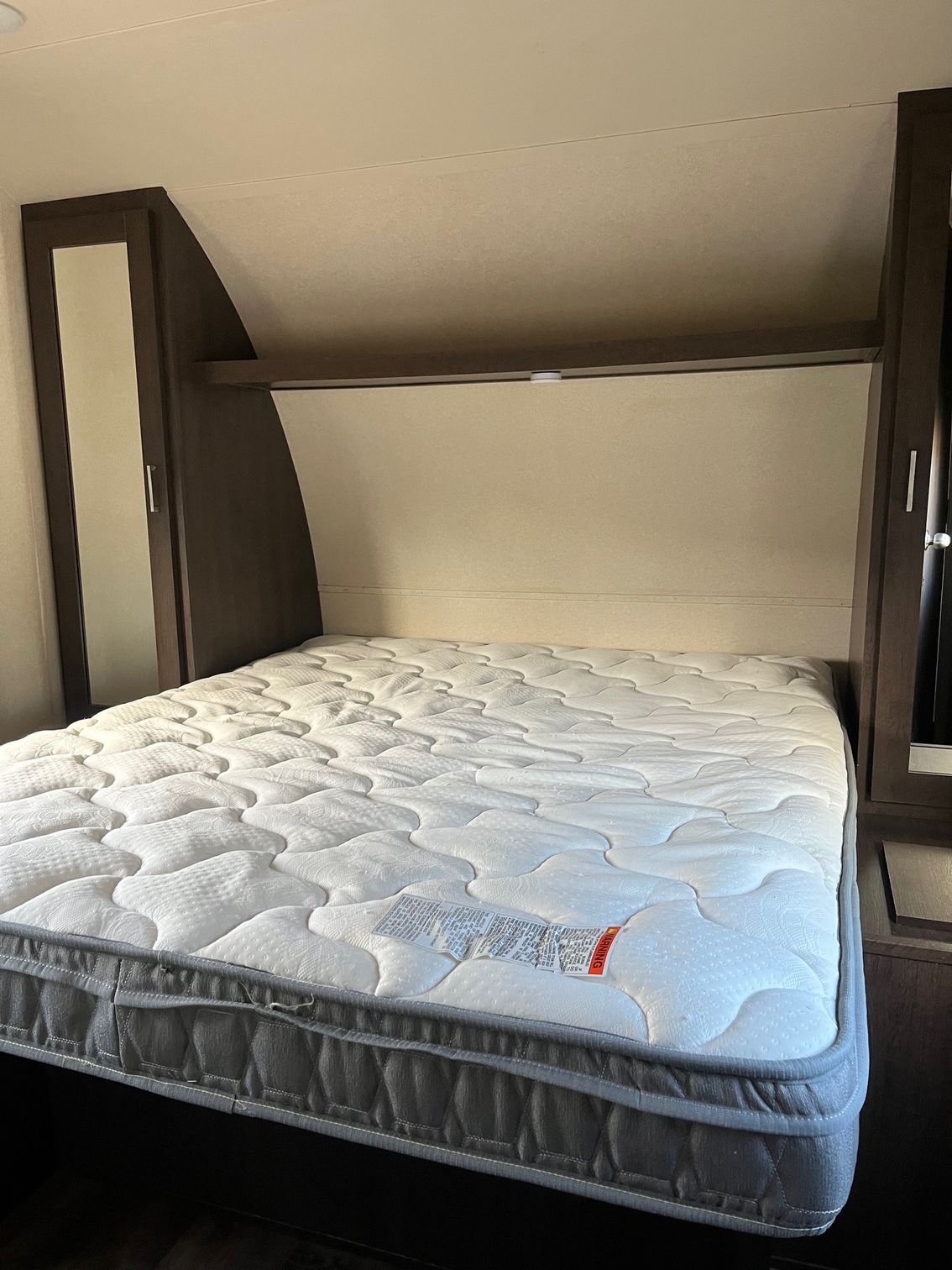 Mattress inside a small camper bed nook with dark wood framing and beige walls