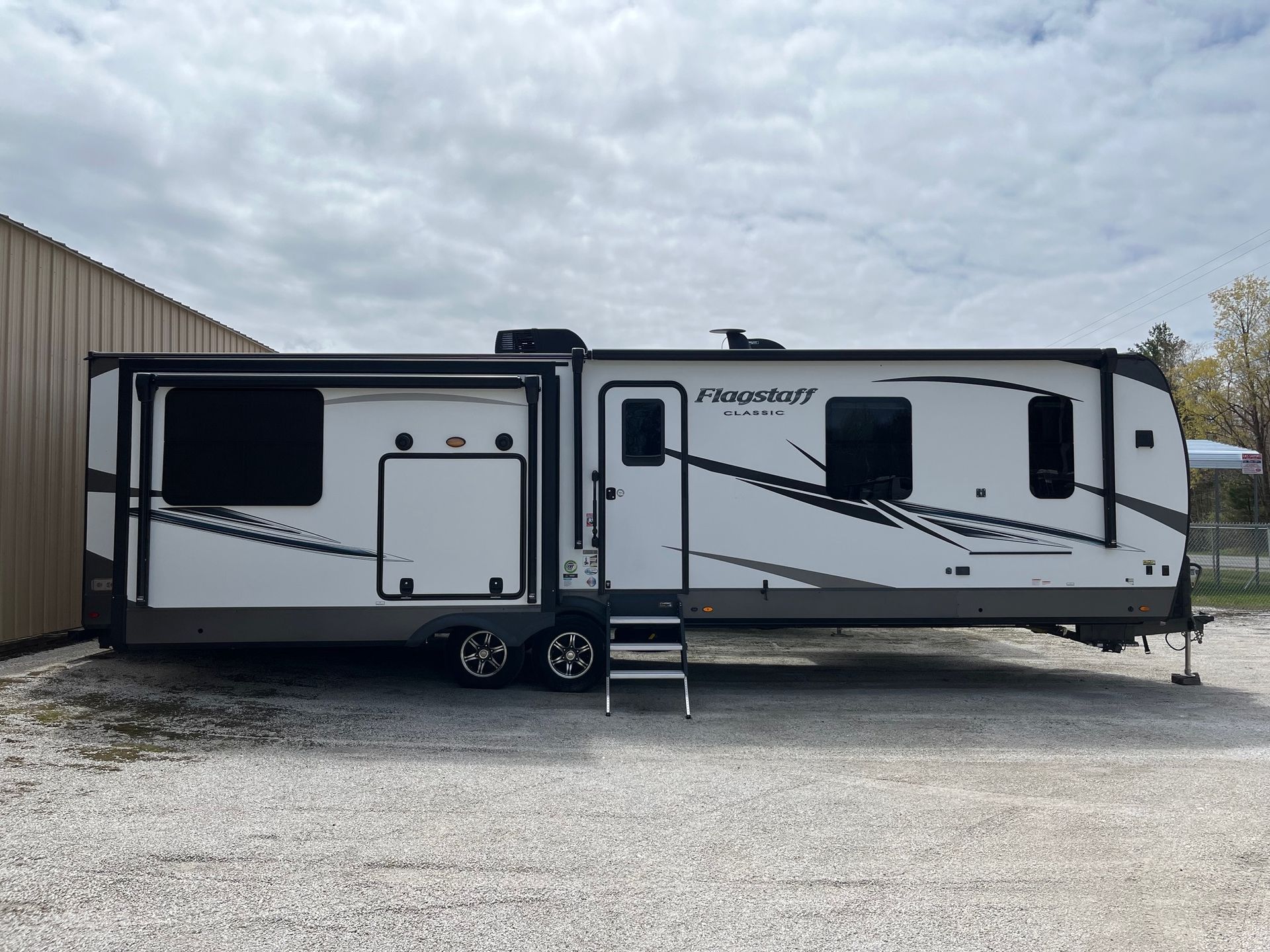 White travel trailer parked on gravel beside a building under a cloudy sky