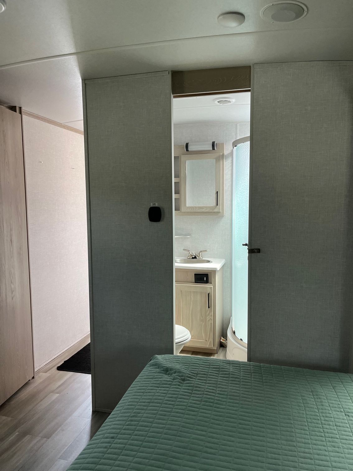 Small bedroom with a bed in foreground and an open doorway to a bathroom with sink and mirror.