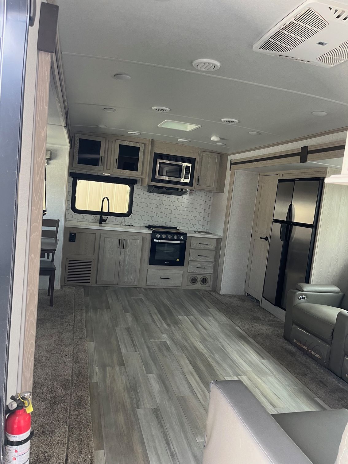 Compact RV interior with kitchen, gray flooring, sofa, and bunk beds near the back.