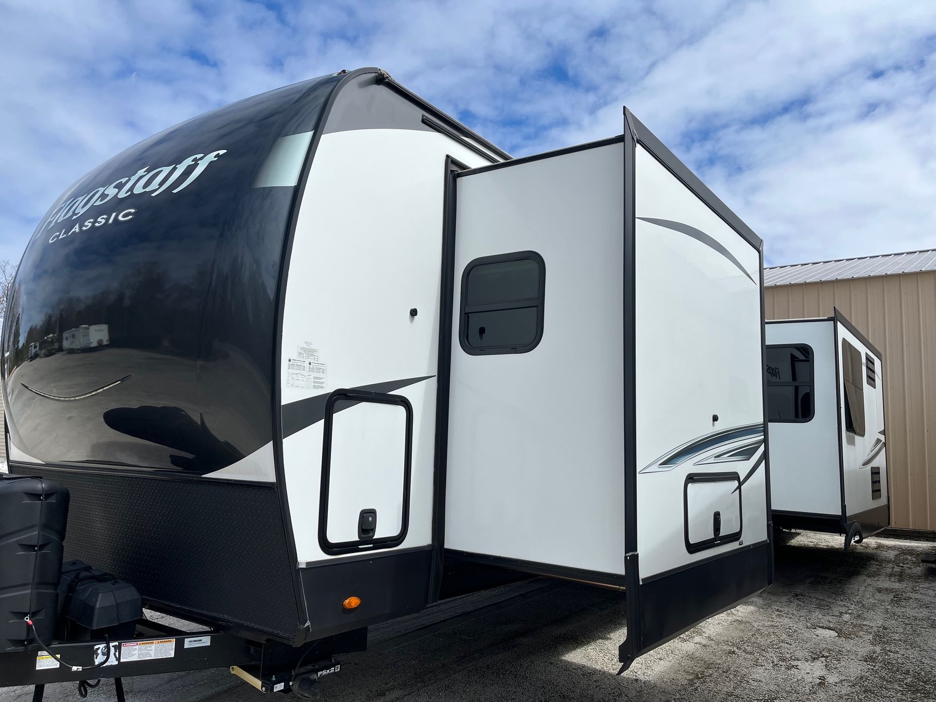 Black-and-white travel trailer with open side door, parked at a campsite under a cloudy sky