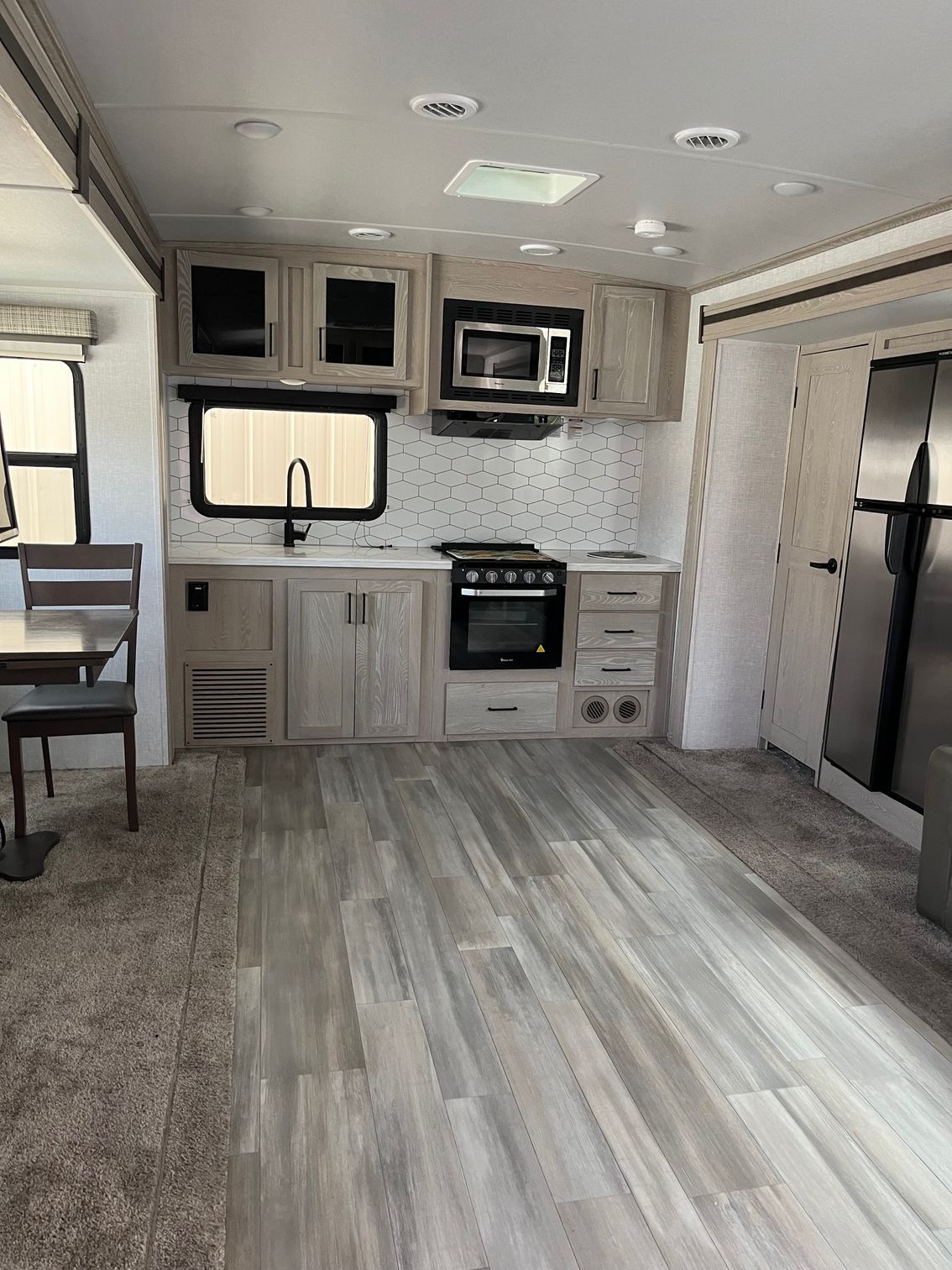 Small RV kitchen and living area with gray cabinets, stove, microwave, and wood-look flooring