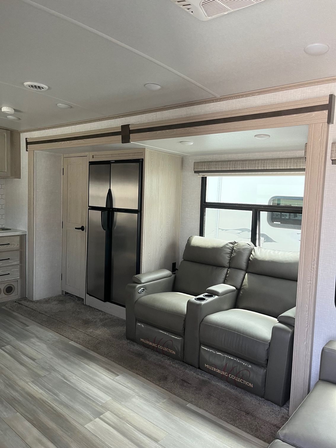 RV interior with gray recliners, a black refrigerator, and large window seating area