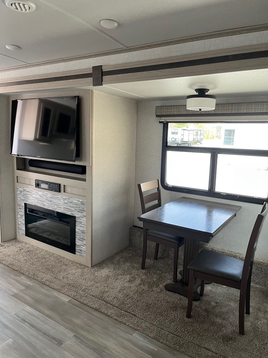 Compact RV interior with fireplace, TV, and a small dining table by a window.