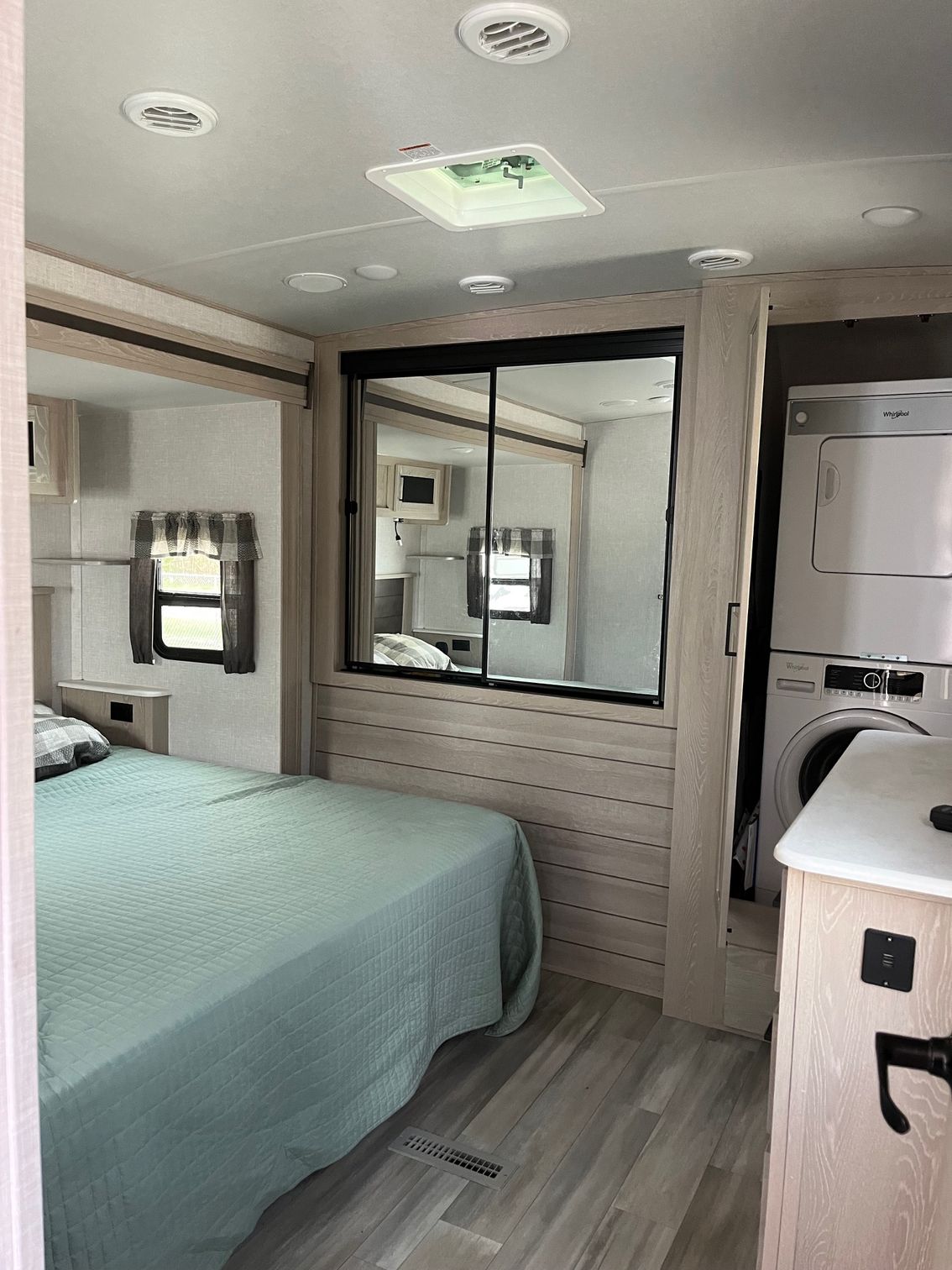 Bright bedroom with teal bedspread, mirrored cabinet, ceiling lights, and an adjoining bathroom door