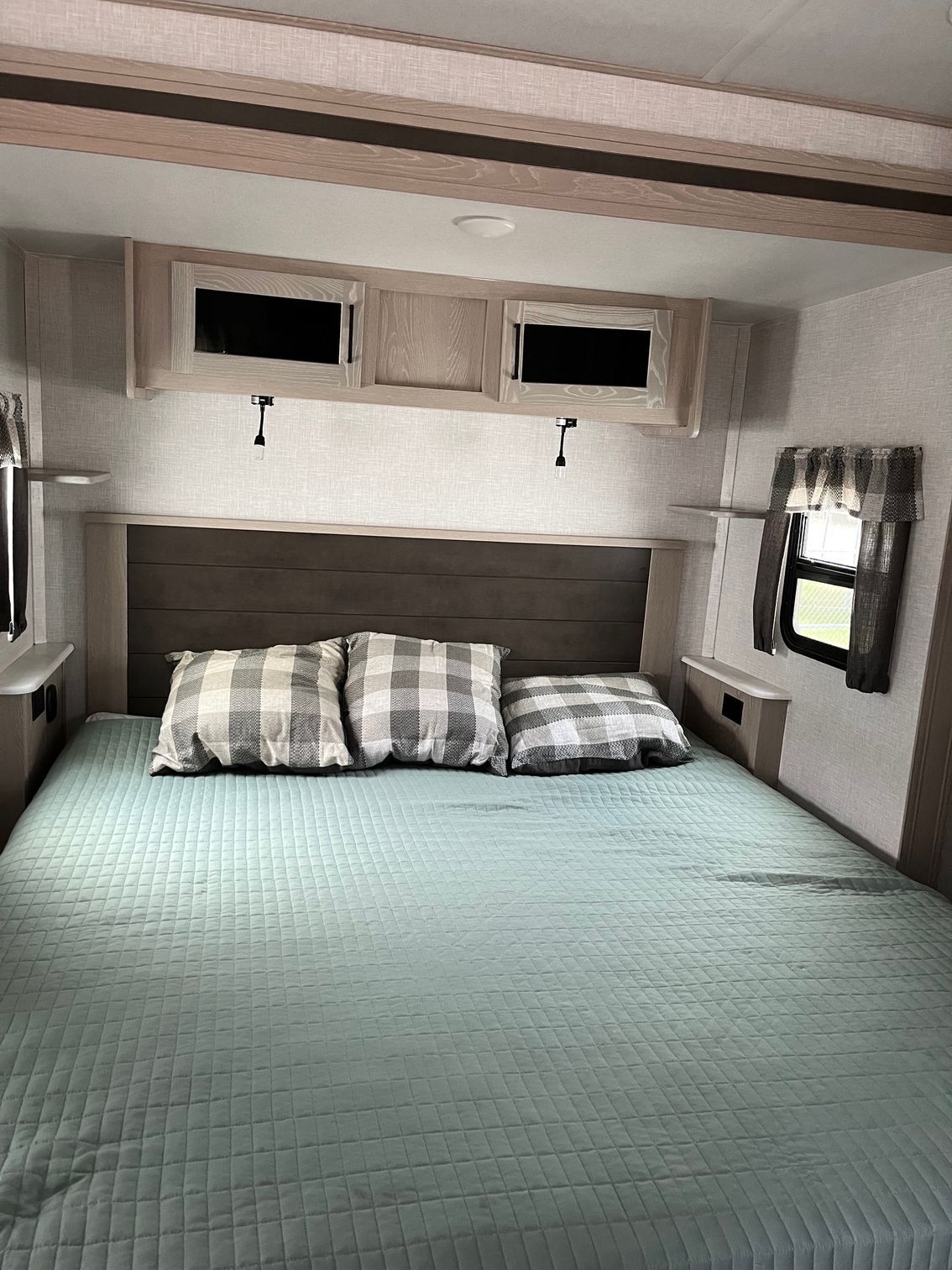 Cozy bedroom with a large bed, plaid pillows, light blue bedding, and wall cabinets above the headboard