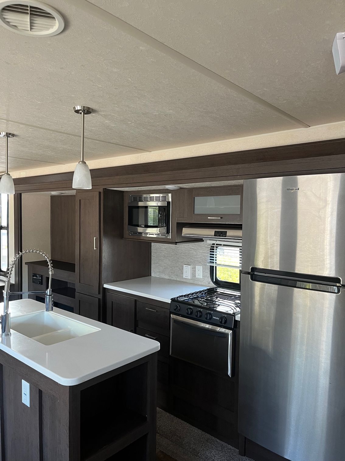 Modern kitchen with stainless steel appliances, dark cabinets, white countertops, and a center island sink