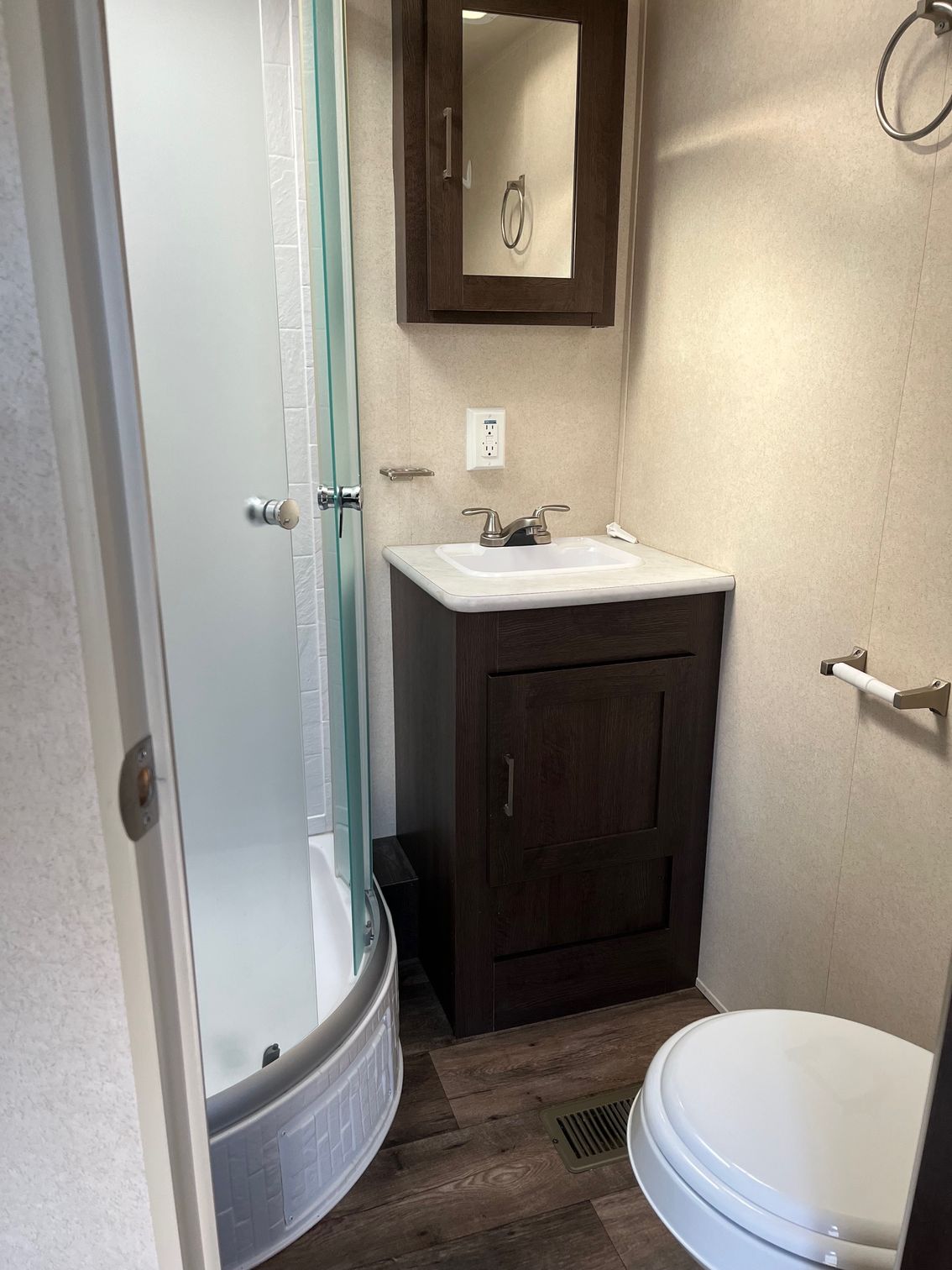 Small bathroom with shower, vanity sink, mirror, and toilet in neutral tones.