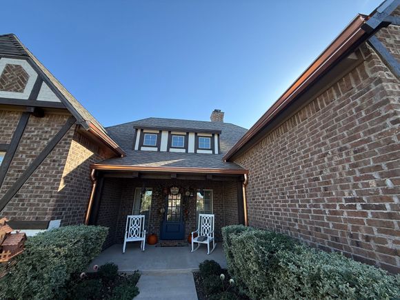 Tan brick house with brown roof and garage door, blue sky.