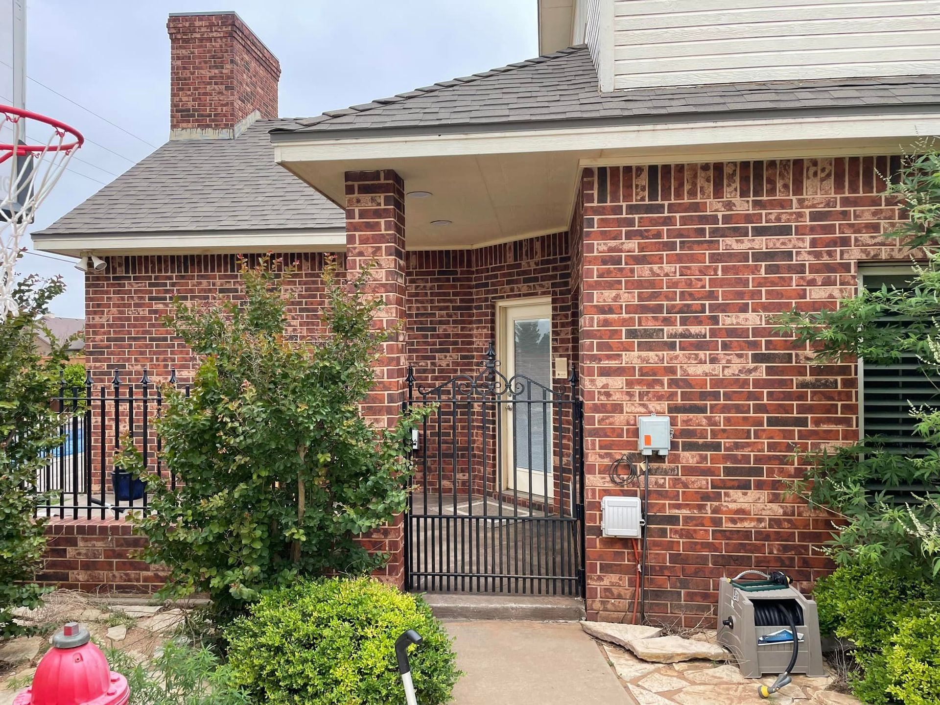 Red brick house with a gated entrance and bushes.