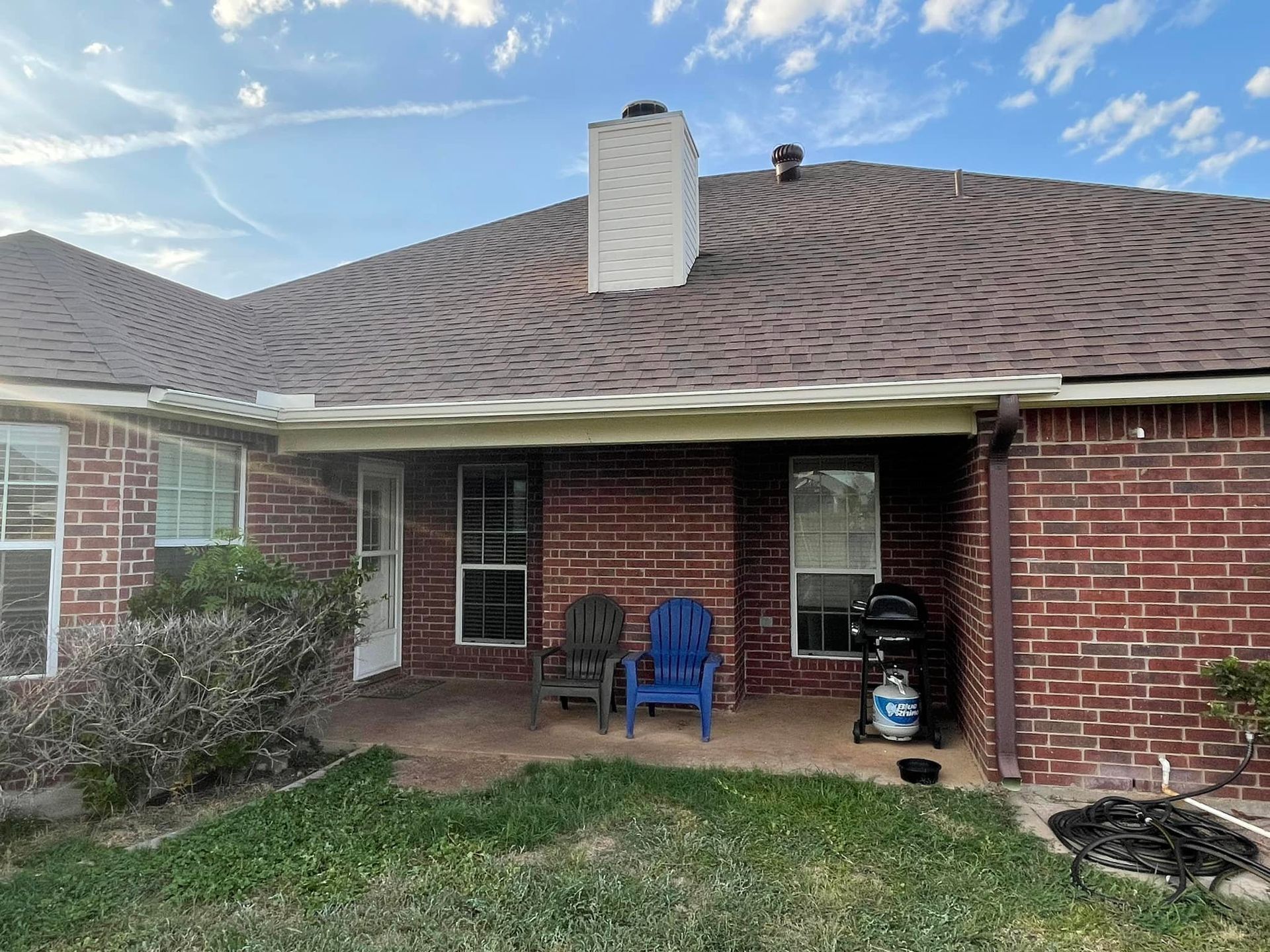 Brick house exterior with a patio, chairs, grill, and chimney against a blue sky.