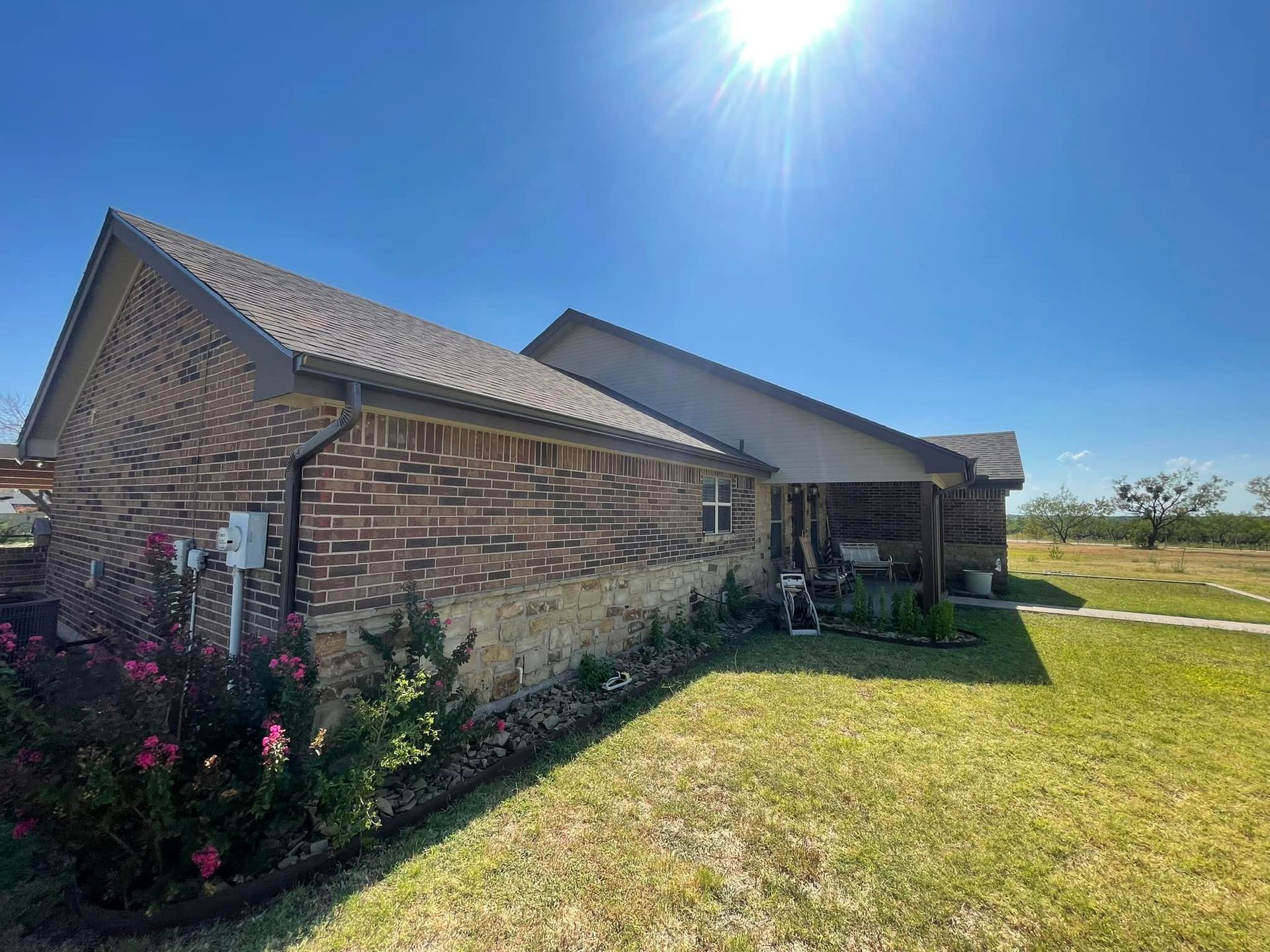 Brick house with dark roof and porch under a bright blue sky.
