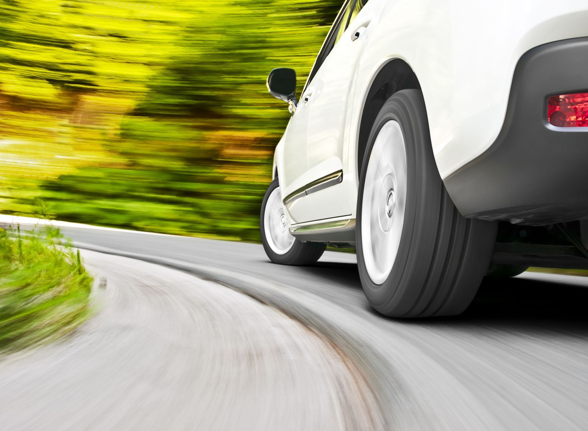 White car driving fast on a curving road past blurred green trees