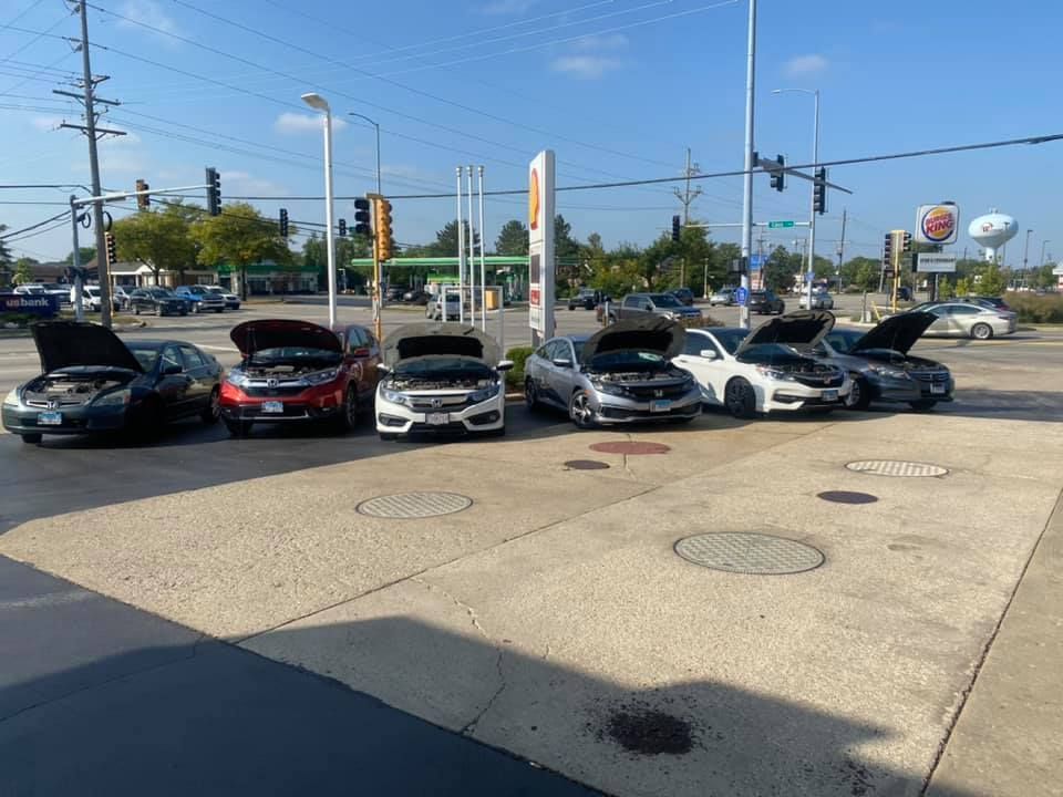 Damaged cars lined up in a parking lot by a street intersection under a clear blue sky.