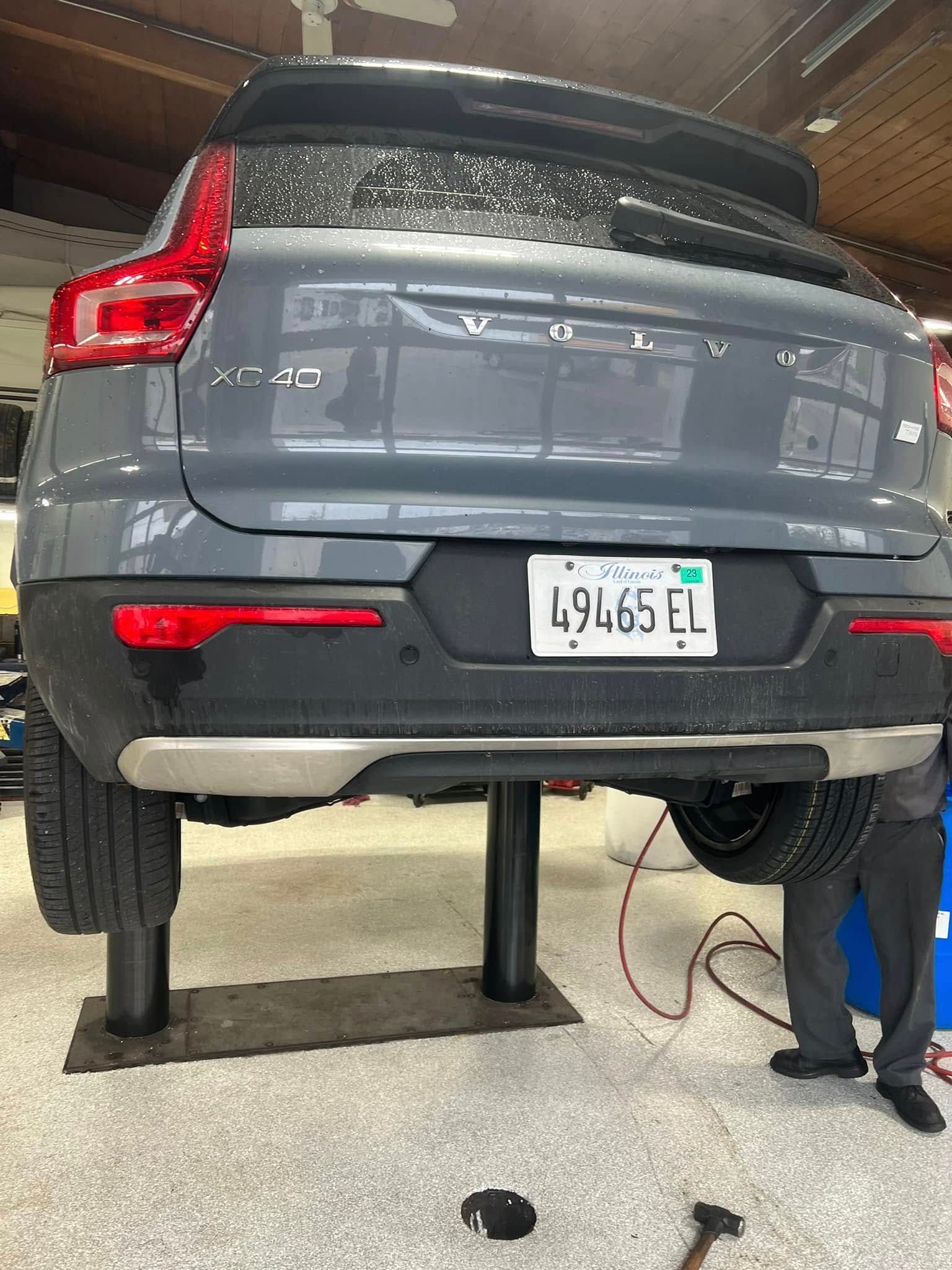 Gray SUV raised on a lift in a garage, with a mechanic working underneath.