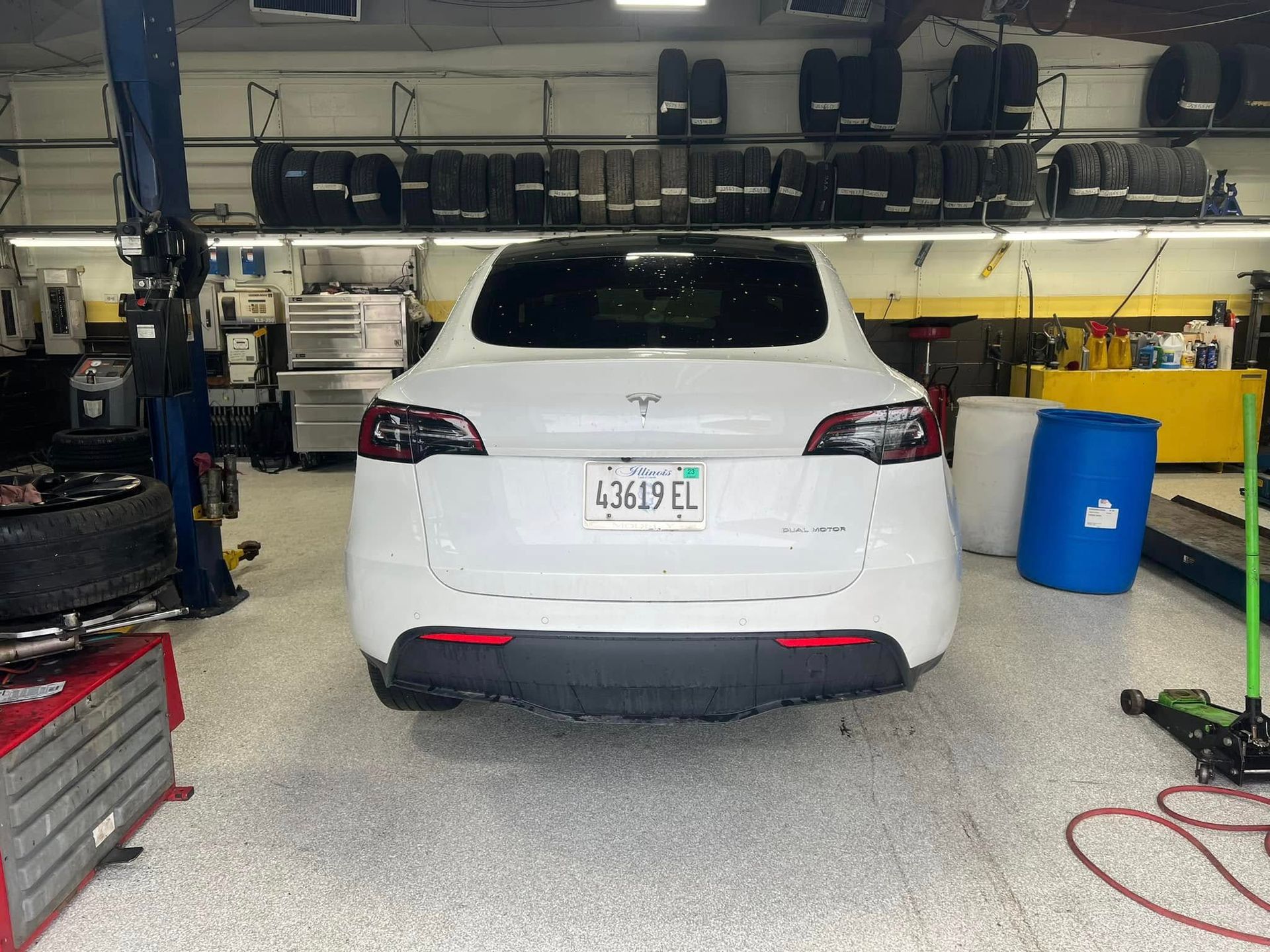 White SUV parked in a garage workshop, seen from the rear, with tools and equipment around it.