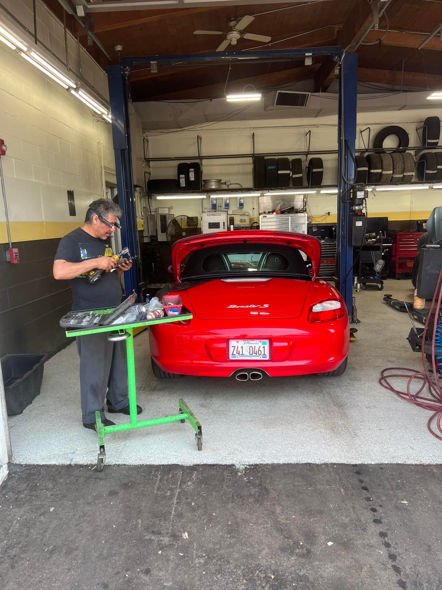 Red sports car in auto shop with a mechanic working beside it on a green stand