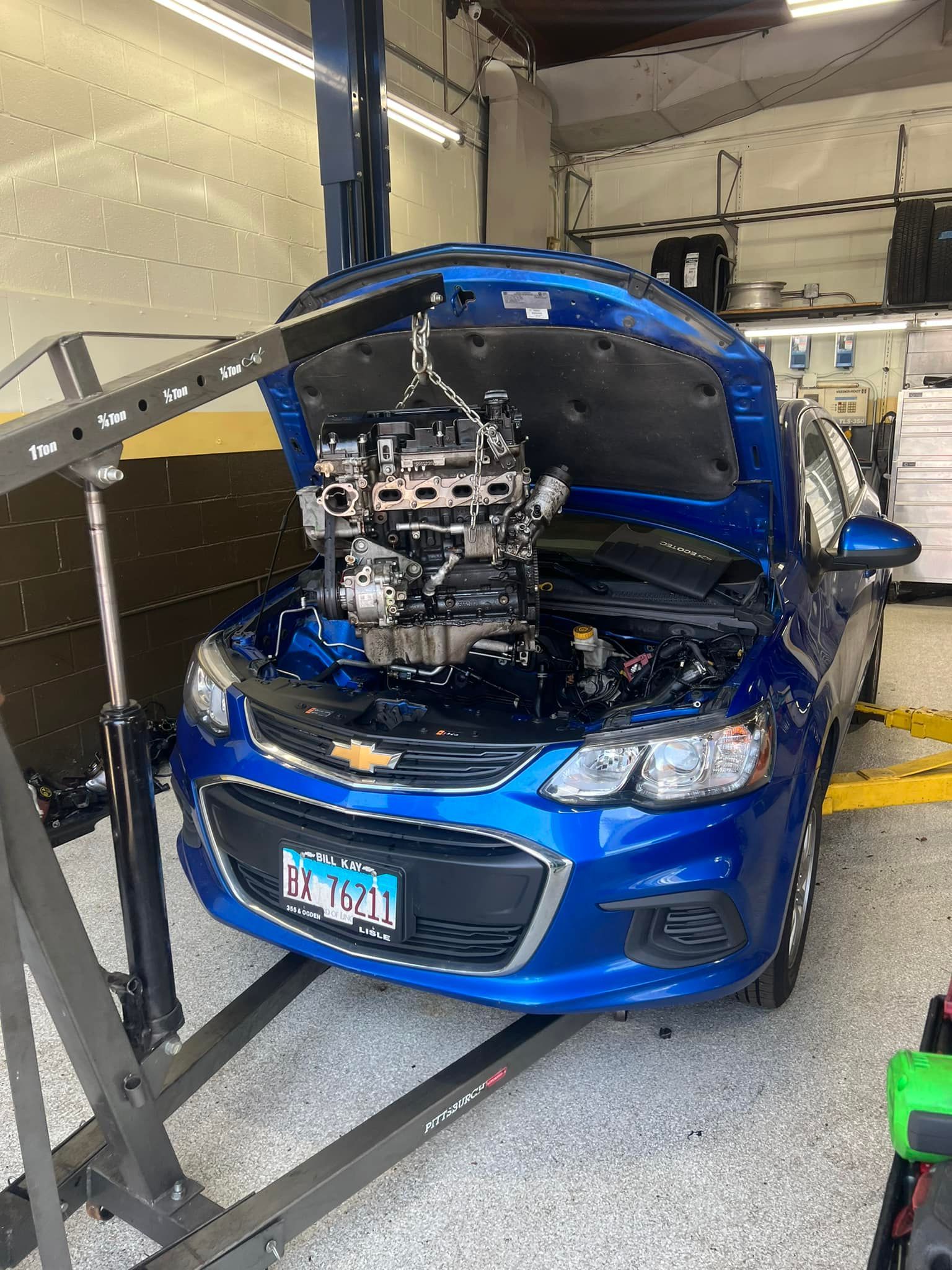 Blue car with hood open, shown on a dynamometer in a garage with testing equipment.