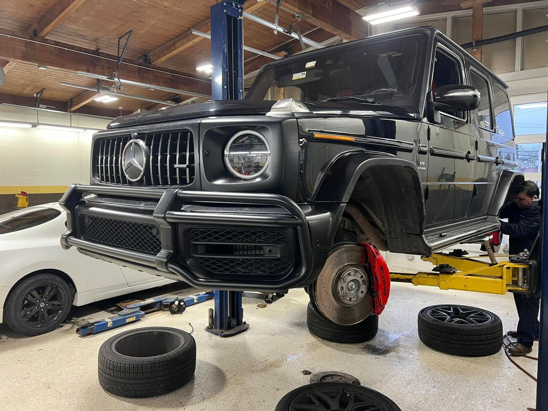 Black Mercedes G-Class lifted in a garage, with wheels off and tires on the floor.