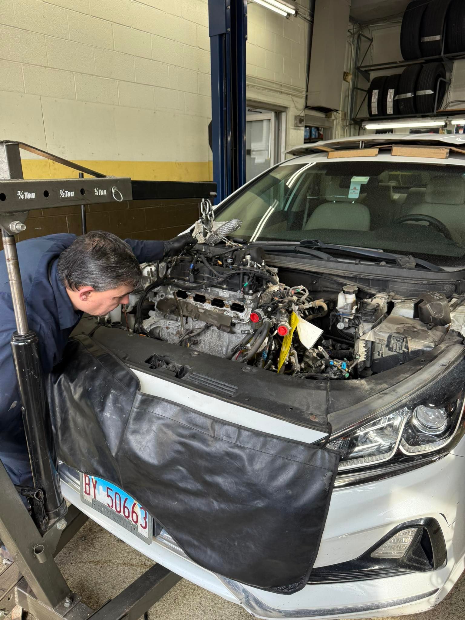 Mechanic inspecting a silver car with hood open in an auto repair shop