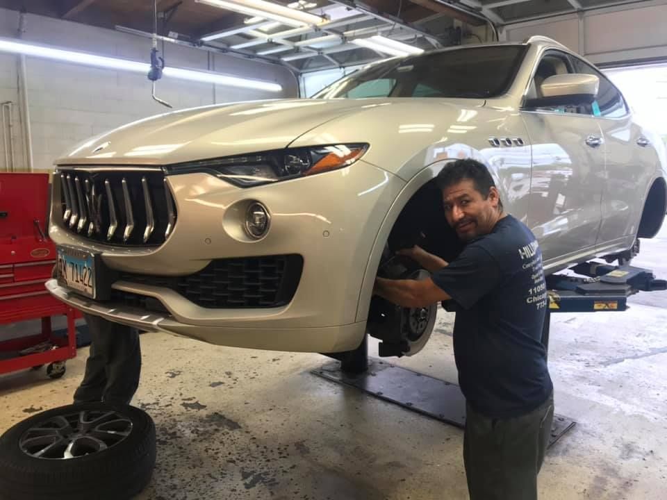 Mechanic working on a white SUV lifted in an auto repair shop