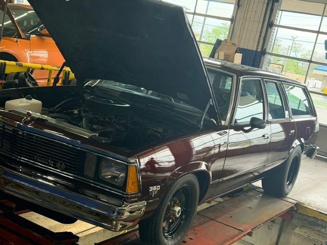 Maroon vintage station wagon on a garage lift with hood open for repair