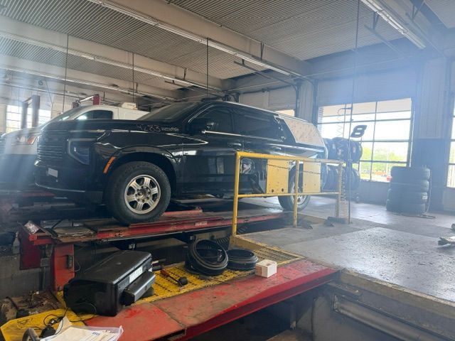 Black car on an auto shop lift inside a garage with yellow safety rails
