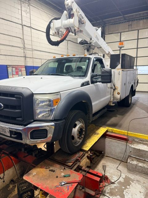 White utility truck with boom lift inside a maintenance garage, parked over a service pit.
