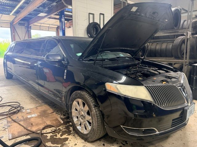 Black limousine with hood open in an auto shop, showing front damage and a wheel lifted off the ground.