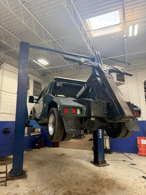 SUV raised on a hydraulic lift in an auto repair shop, with its rear wheels hanging off the ground.