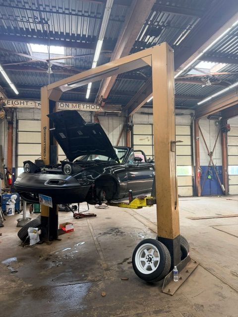 Black car lifted by a wooden gantry in a workshop, with tools and a wheel nearby.