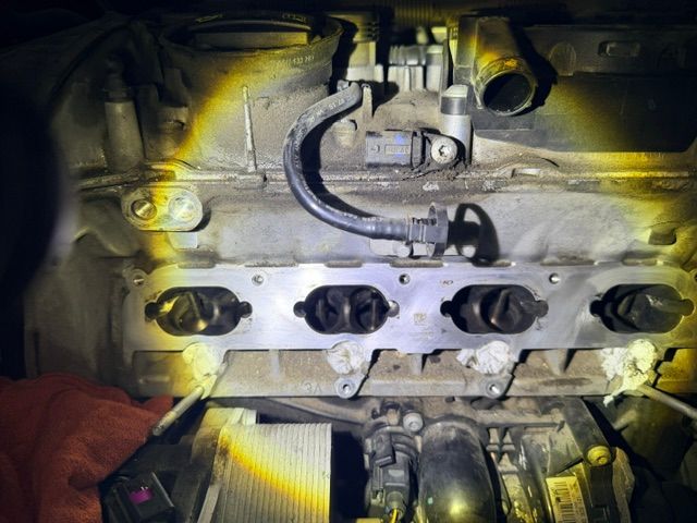 Engine bay interior with metal components, hoses, and four dark circular openings lit by a flashlight