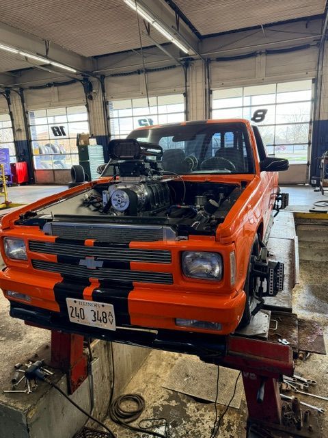 Orange classic pickup truck on a lift inside a garage, with engine exposed