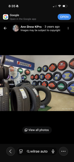 Tire shop display with stacked tires and colorful wheel rims on the wall, viewed on a phone screen
