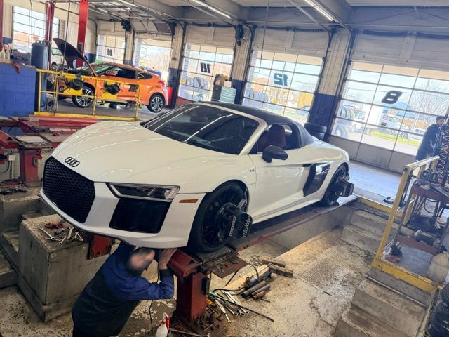 White Audi sports car on a lift in an auto shop, with a mechanic working underneath