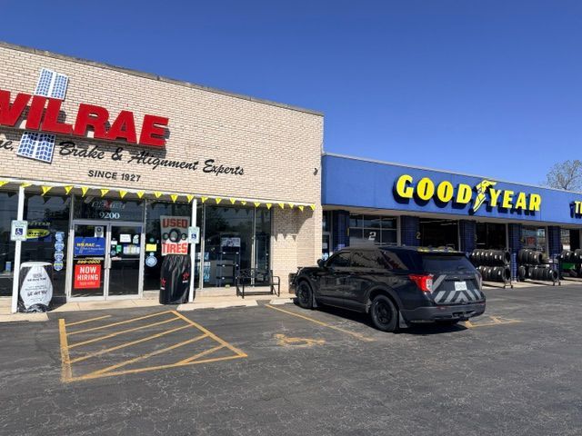 Auto repair storefronts: Wilrae and Goodyear signs on a sunny strip mall, with a black SUV parked outside