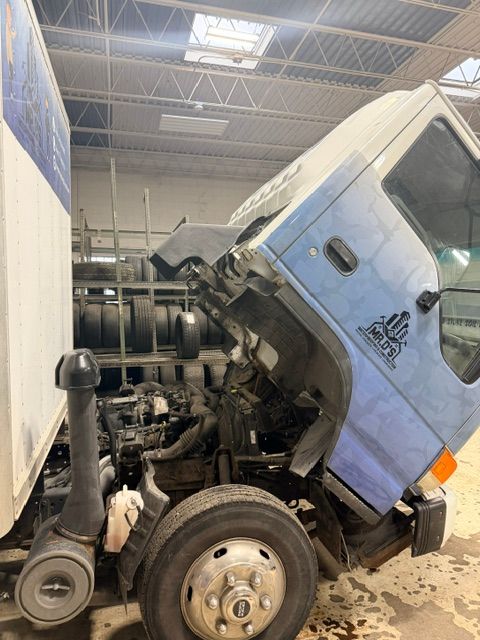 Damaged blue semi-truck cab crushed against another vehicle inside a warehouse-like garage