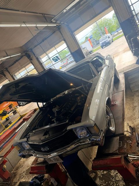 Silver classic car on a lift in an auto shop, hood open for repair