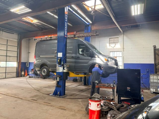 Mechanic working on a dark van inside an auto repair garage with a lift and tools.