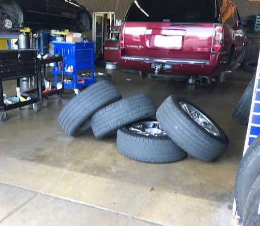 Four tires on a garage floor beside a red SUV in a workshop