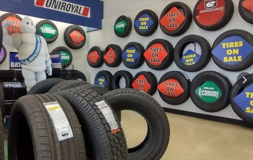 Tire shop display with stacked tires and colorful wall-mounted tire signs, including “TIRES ON SALE” and “UNIROYAL”