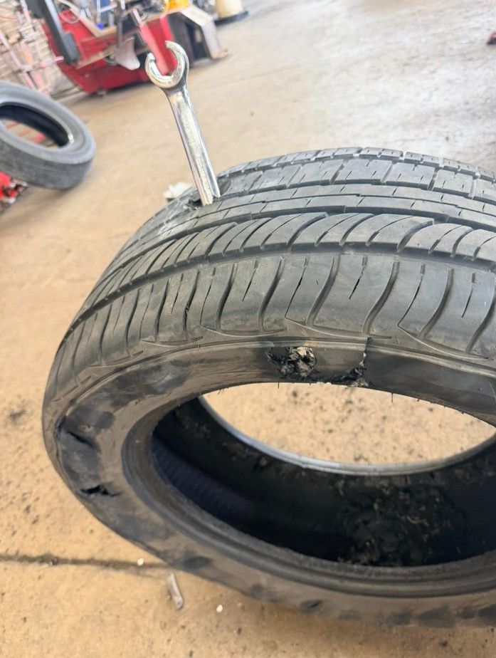 Damaged car tire with a puncture and tread wear, leaning in a workshop.